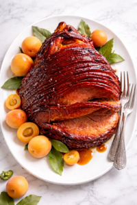 apricot molasses glazed ham on white platter with fresh apricots and glossy sticky glaze on marble countertop