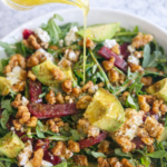 arugula beet salad with avocado goat cheese candied walnuts and honey lemon vinaigrette being poured