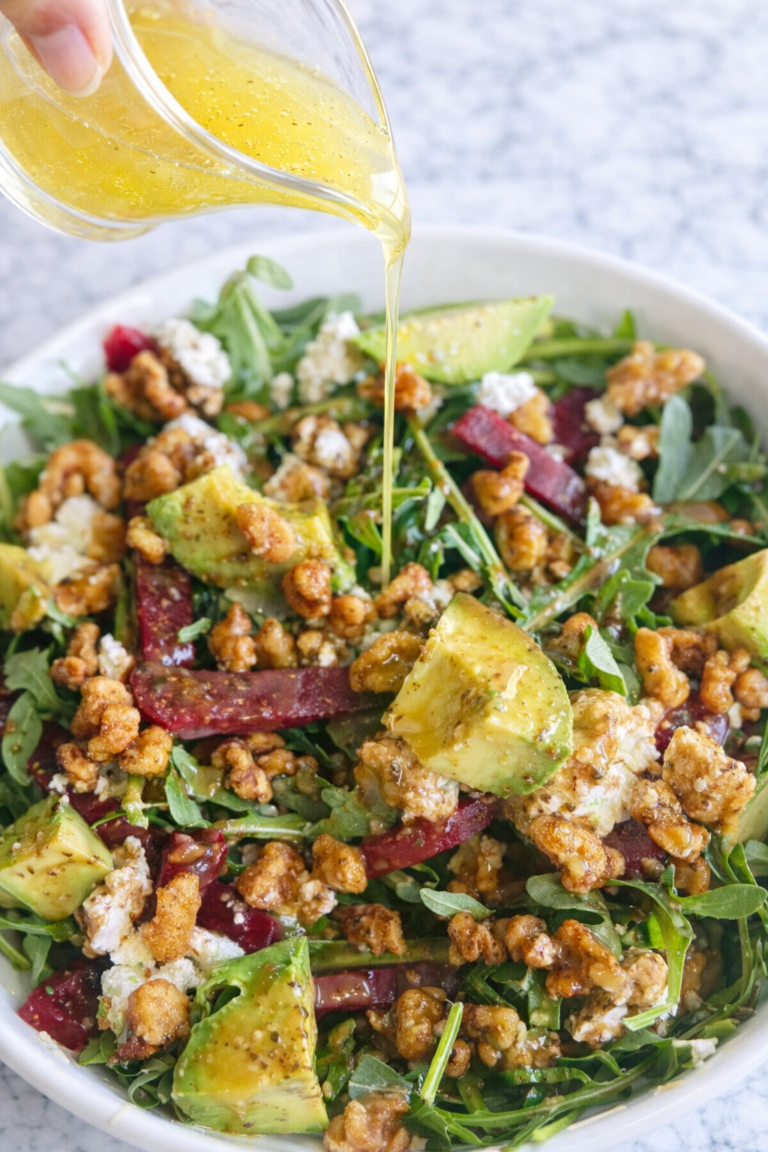 arugula beet salad with avocado goat cheese candied walnuts and honey lemon vinaigrette being poured
