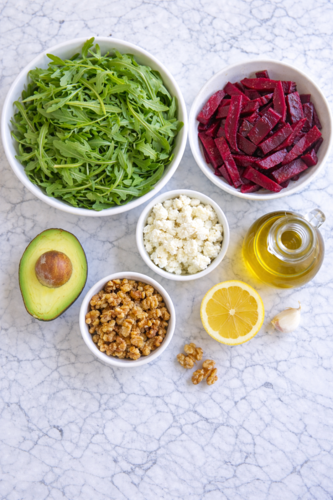 flat lay ingredients for arugula beet salad with avocado goat cheese candied walnuts lemon garlic and olive oil on marble counter