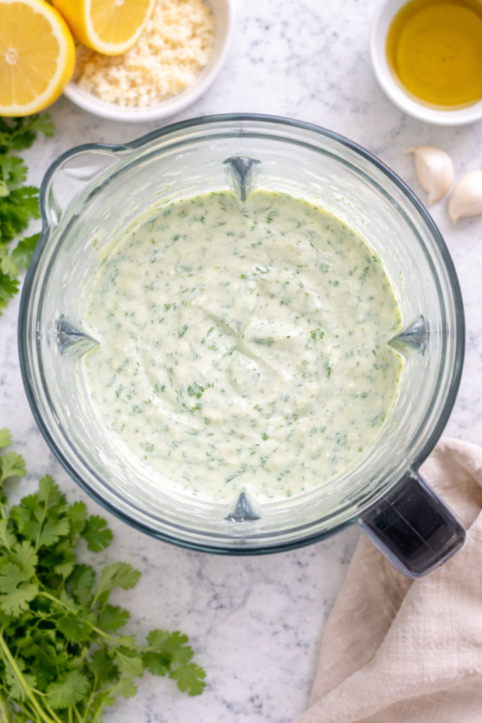 Bird’s-eye view of creamy Asiago cilantro garlic yogurt dressing blended in a blender on a white marble countertop.