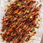 crispy billion dollar bacon drizzled with Asian garlic chili oil and topped with sliced scallions on wrinkled parchment paper