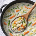 Creamy asparagus and chicken chowder with potatoes and carrots in a black pot on a marble countertop