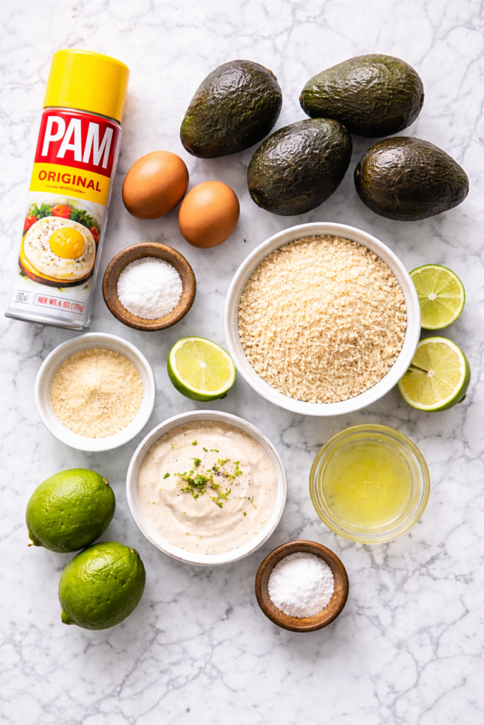 Flat lay of ingredients for crispy baked avocado fries including avocados, panko breadcrumbs, eggs, limes, ranch dressing, and PAM cooking spray on a marble countertop.