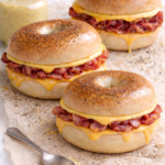 Bacon egg and cheese bagel sandwiches with dill mustard mayo on parchment paper, sprinkled with pepper and dried dill