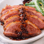 Spoon drizzling balsamic honey sauce over sliced pan seared duck breast with crispy skin on white plate