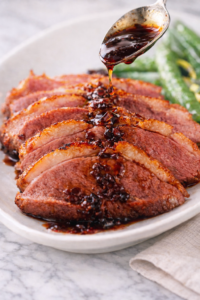Spoon drizzling balsamic honey sauce over sliced pan seared duck breast with crispy skin on white plate