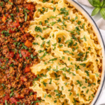 homemade bolognese sauce with mafalde pasta in white enamel skillet on marble countertop