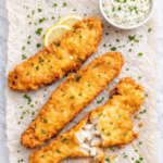 crispy beer battered fish fry on wrinkled parchment paper with homemade tartar sauce and lemon slices