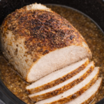sliced bistro butter turkey breast cooking in a crockpot with buttery seasoned broth