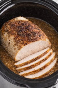 sliced bistro butter turkey breast cooking in a crockpot with buttery seasoned broth