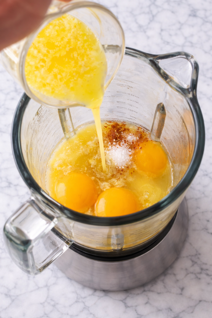 Bird’s eye view of hollandaise sauce ingredients blending in a blender with egg yolks and melted butter