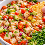 Tortilla chip scooping Bloody Mary ceviche with shrimp, white fish, avocado, tomatoes, red onion, and Clamato sauce