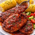 Boneless pork chops on a plate with corn on the cob while rhubarb barbecue sauce is being spooned over the top
