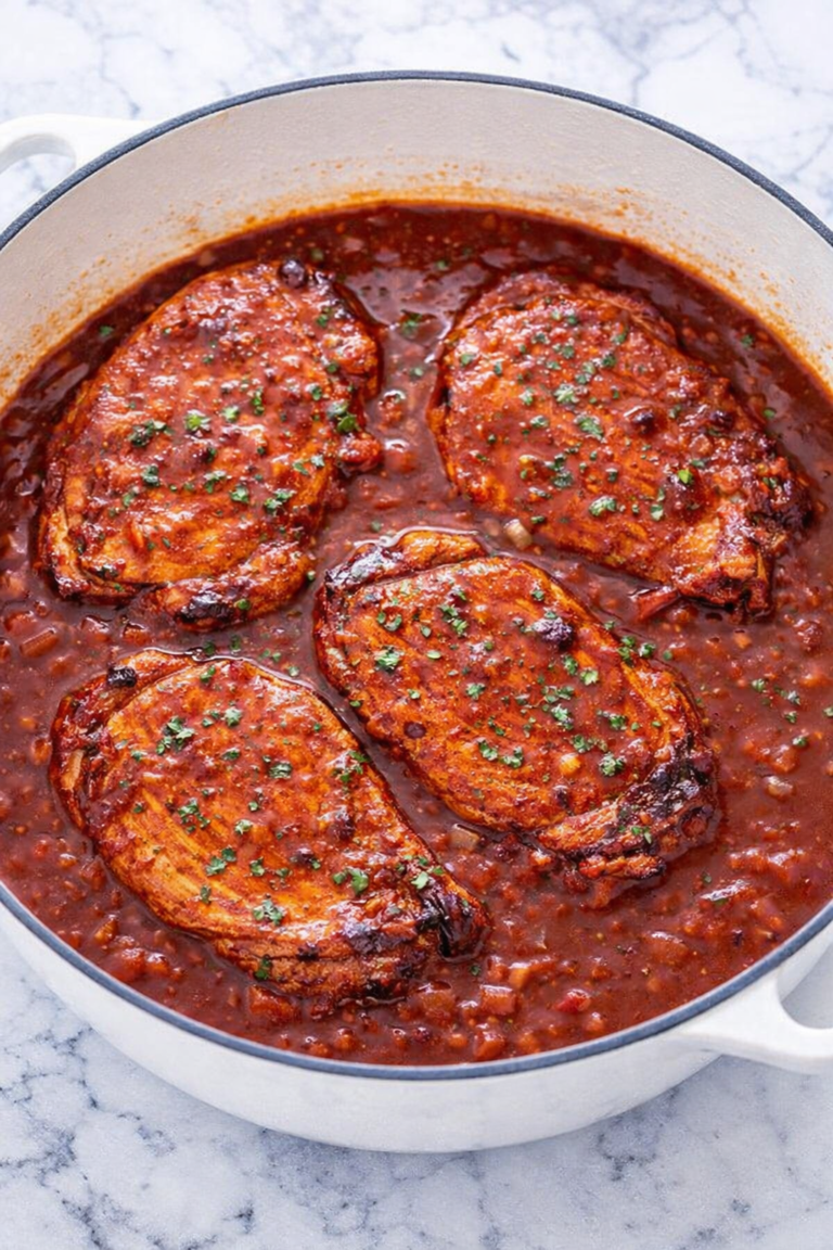 Boneless pork chops simmering in smooth rhubarb barbecue sauce in a white Dutch oven on a marble counter