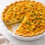 slice of breakfast pie with hash browns bacon eggs and crunchy cornflake topping in a white pie dish on marble counter