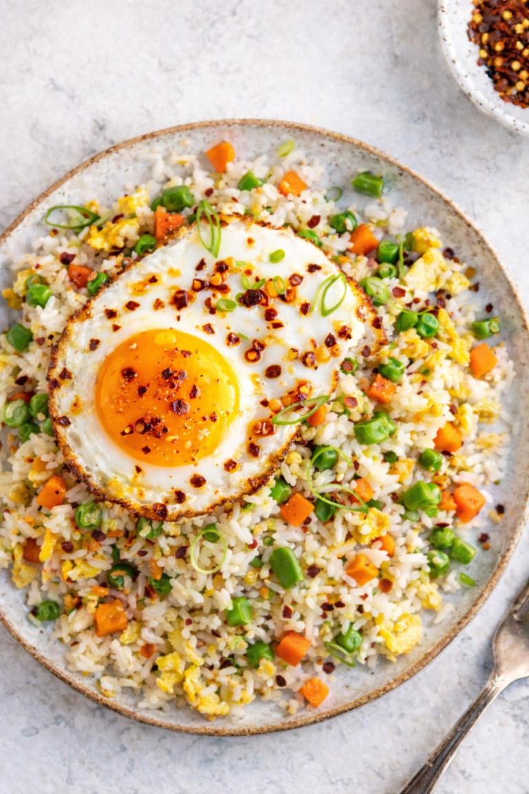 Budget egg fried rice topped with a crispy fried egg and chili crisp on a handmade pottery plate over a marble countertop.
