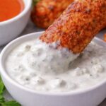 Buffalo chicken roller dipped into creamy blue cheese dressing with celery and carrot sticks in the background