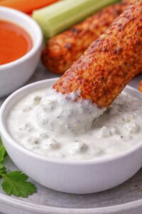 Buffalo chicken roller dipped into creamy blue cheese dressing with celery and carrot sticks in the background