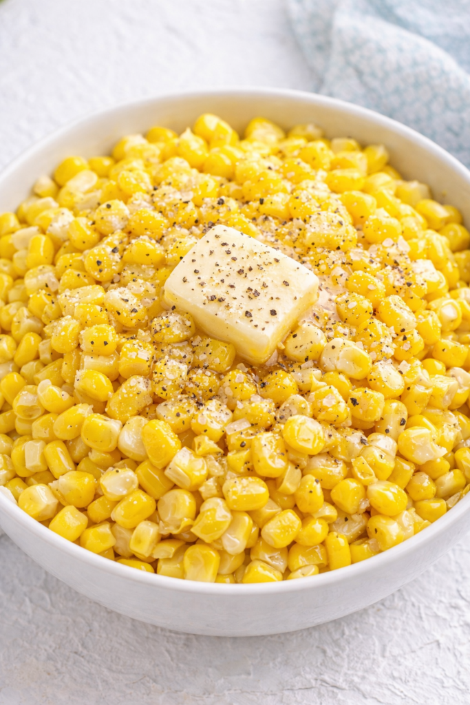 Canned corn in a white bowl with melting butter and sprinkled salt and black pepper