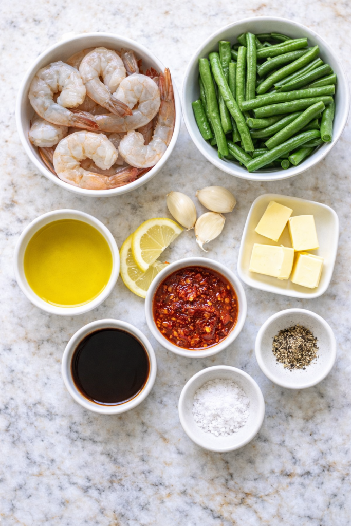 Vertical flat lay of ingredients for Calabrian chili garlic butter shrimp and green bean stir fry on white marble countertop