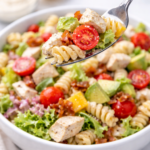 fork scooping california chicken club pasta salad with chicken bacon avocado and tomatoes from white bowl on marble counter
