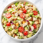 California chicken club pasta salad in a white bowl with bacon, chicken, avocado, and tomatoes on a marble countertop
