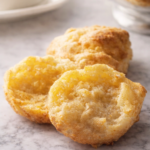 golden homemade cheddar biscuits cut open on a white marble countertop with melted butter inside