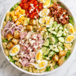 chef salad pasta salad with rotini ham turkey cheese eggs cucumber and creamy dressing in white bowl on marble counter
