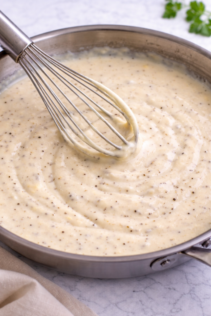 creamy dijon parmesan sauce being whisked in a stainless steel pan