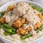 Chicken fried steak mashed potato bowl with green beans and pepper gravy in a white bowl on a marble countertop