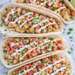 Chicken tacos topped with fresh rhubarb salsa, crema drizzle, and cotija cheese on a marble counter