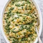 chimichurri chicken casserole with melted cheese, rice, and parsley chimichurri sauce in a white baking dish on a marble counter