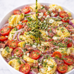 chimichurri roast beef tortellini pasta salad with fresh herbs being drizzled over top