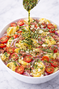 chimichurri roast beef tortellini pasta salad with fresh herbs being drizzled over top