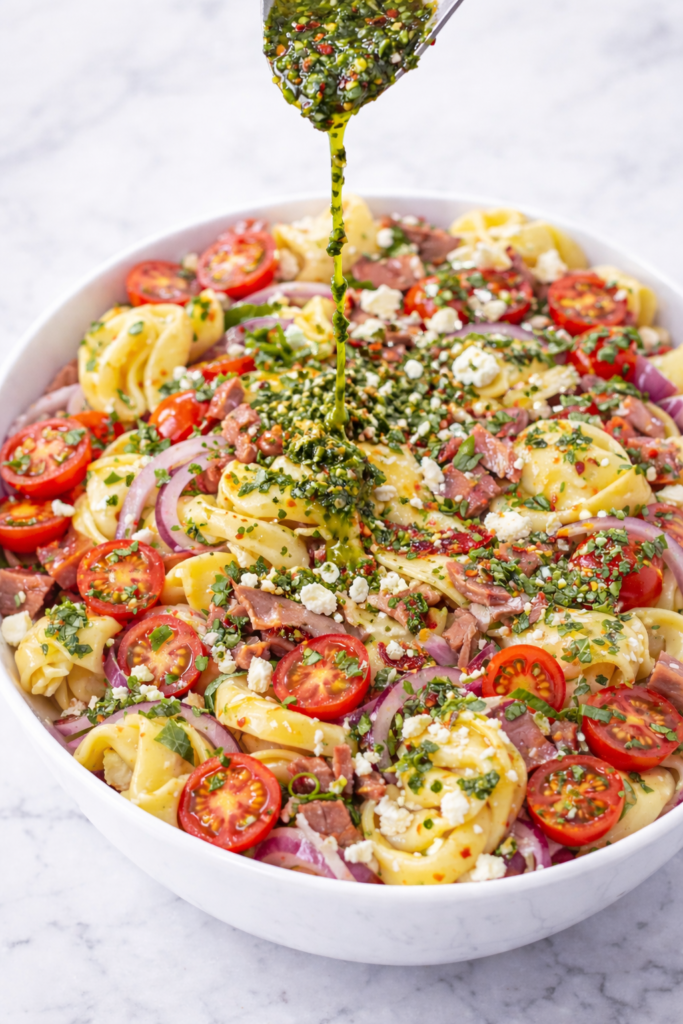 chimichurri roast beef tortellini pasta salad with fresh herbs being drizzled over top