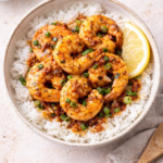 Rice bowl topped with chipotle garlic herb shrimp in a buttery sauce, garnished with green onions and served with a lemon wedge.