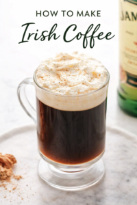 Homemade Irish coffee in a simple clear glass mug topped with lightly whipped cream on a marble countertop