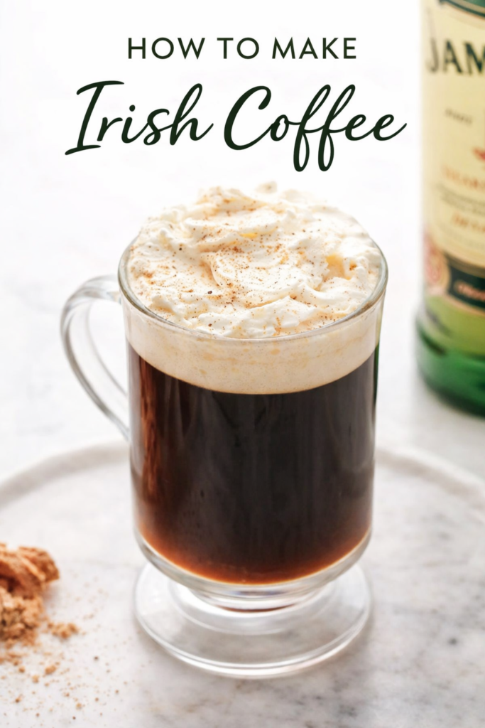 Homemade Irish coffee in a simple clear glass mug topped with lightly whipped cream on a marble countertop