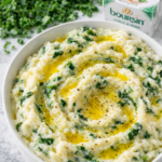 Creamy Irish colcannon with kale and Boursin cheese topped with melted butter in a white bowl on a marble counter