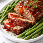 Juicy copycat Cracker Barrel meatloaf with a sweet tangy glaze, sliced and served with green beans on a white platter over a light marble counter
