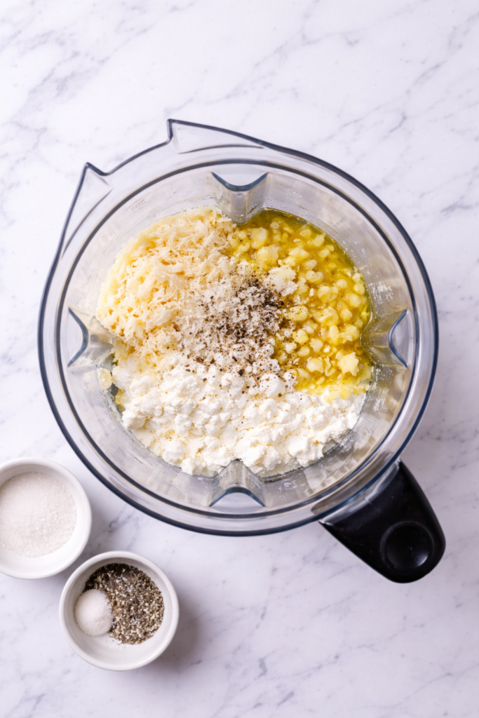cottage cheese alfredo ingredients in blender with melted butter and garlic before blending on marble counter
