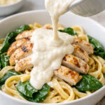 creamy cottage cheese alfredo sauce being poured over chicken fettuccine with spinach in white bowl