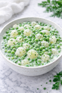 creamed peas and pearl onions in a creamy garlic herb sauce in a white bowl