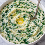 creamy creamed spinach mashed potatoes in a white bowl with butter and spinach on a marble counter