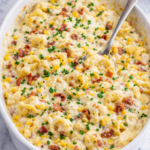 creamy corn and bacon tortellini bake in white dish with cheese sauce on marble counter