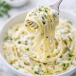 Fork twirling creamy fettuccine pasta with artichokes and blue cheese over a white bowl