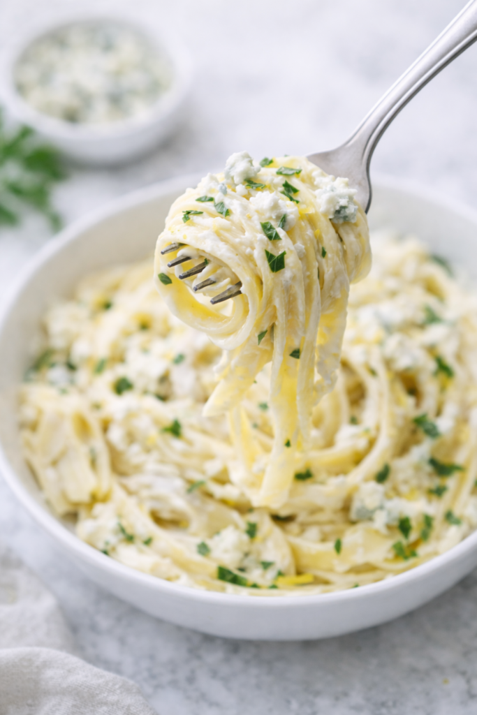 Fork twirling creamy fettuccine pasta with artichokes and blue cheese over a white bowl