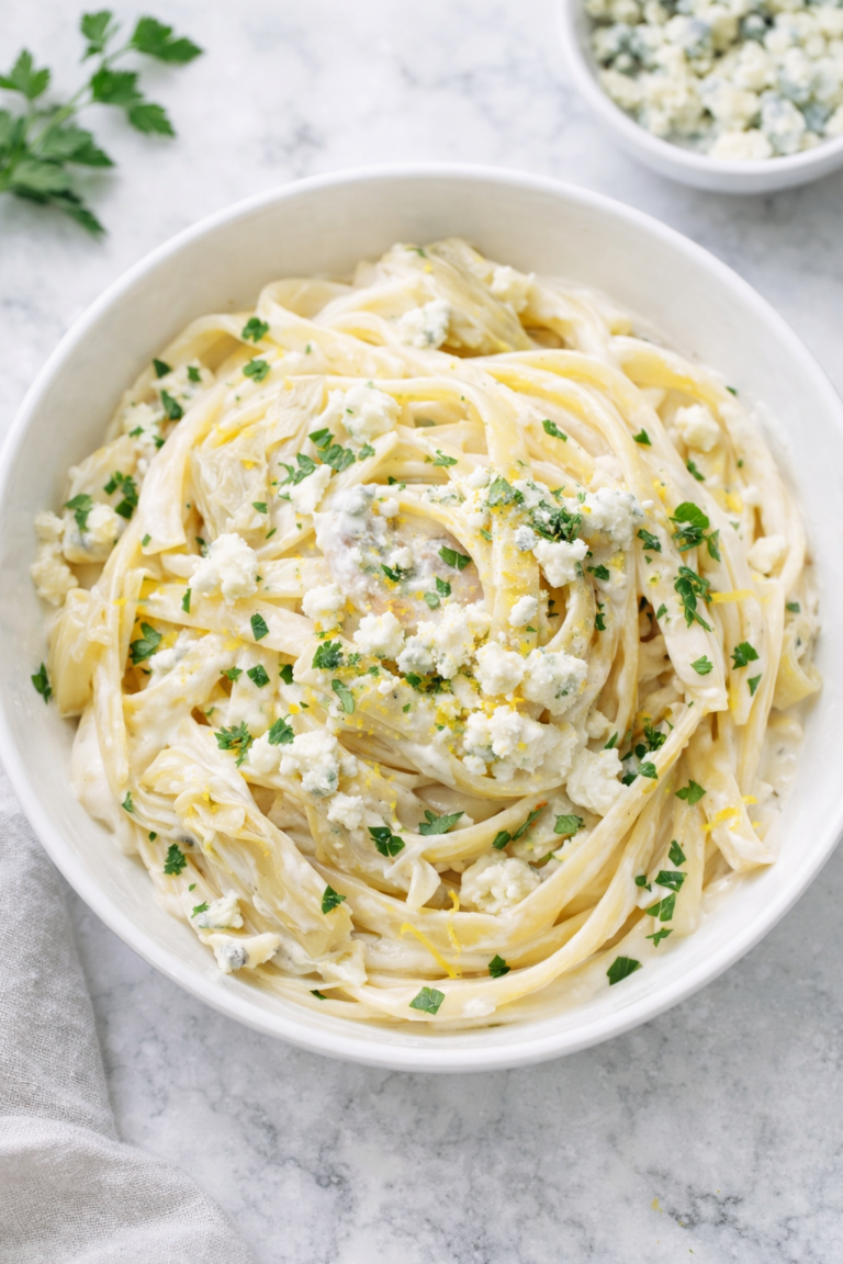 Creamy fettuccine pasta with artichokes and blue cheese in a white bowl on a marble countertop