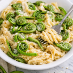 creamy fiddlehead fern pasta in white bowl on marble counter with fork